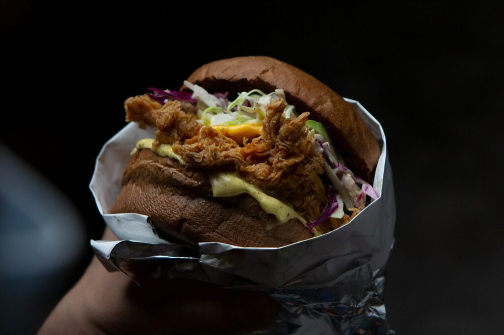 A hand presents a sandwich overflowing with colorful toppings, captured in a creative food photography setting.