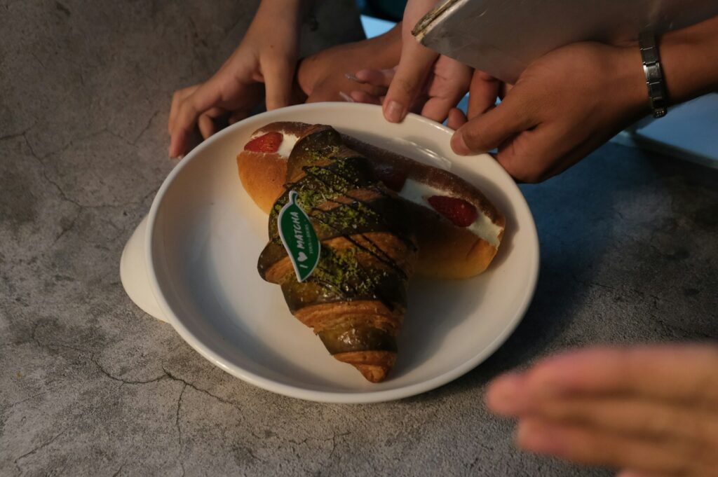 A hand presents a plate with a croissant and a hot dog, highlighting the artistry of food photography.
