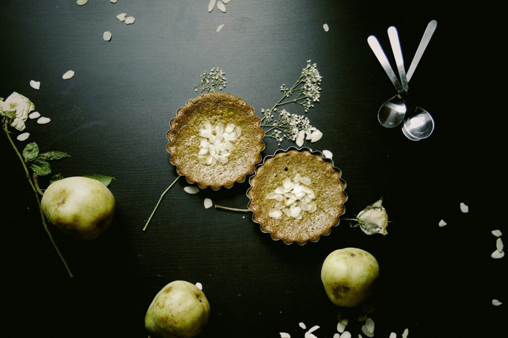 A creative food photograph featuring two pies decorated with vibrant flowers and leaves on a wooden table.