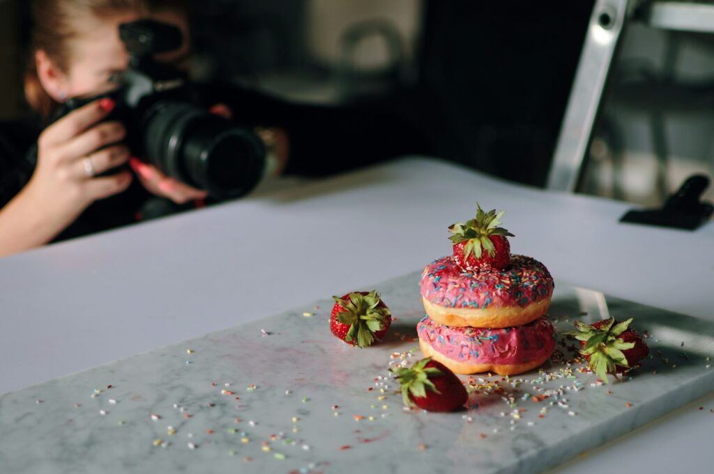 A professional food photographer captures a colorful donut topped with sprinkles, focusing intently on the shot.