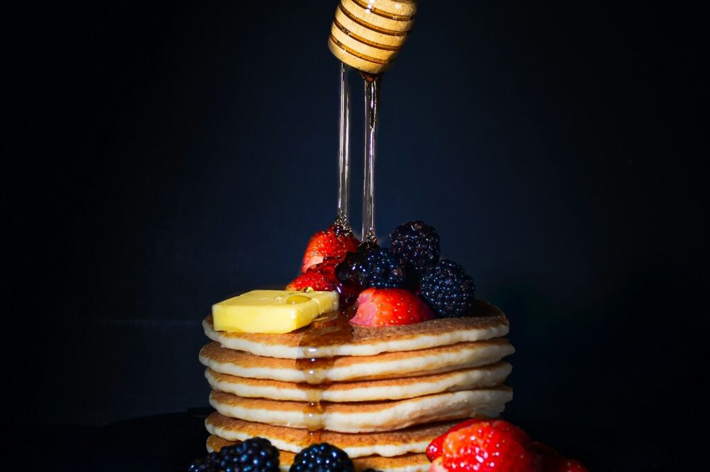 Delicious pancakes with syrup and assorted berries served on an elegant black plate.