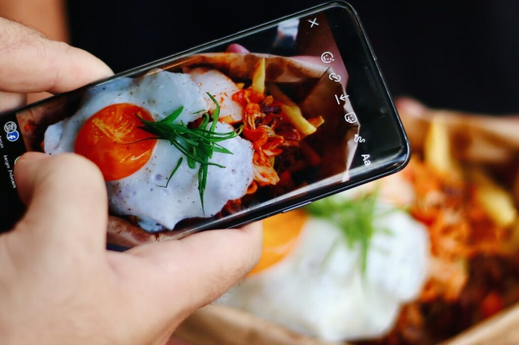 A person using a smartphone to take a vertical photo of a meal, highlighting the art of food photography.