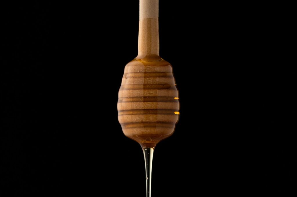 A wooden stick with honey dripping from it, highlighting eco-conscious food photography and a focus on natural ingredients.