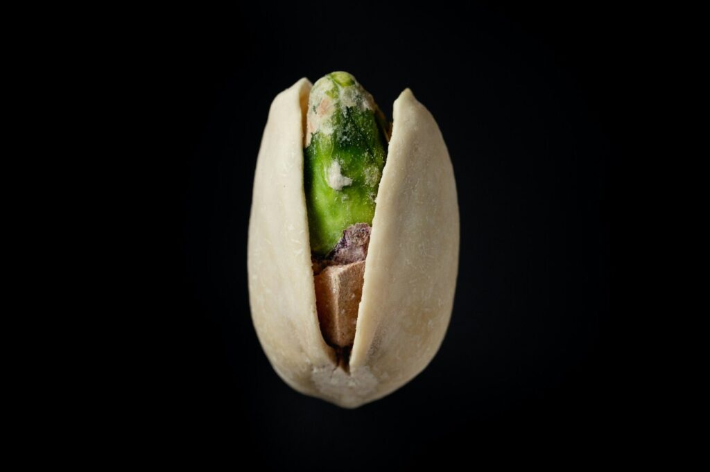 Close-up of a pistachio nut against a black background, highlighting its details in a Singaporean food photography setting.