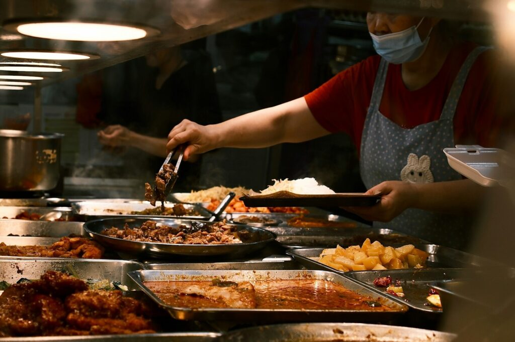 A woman in a mask serves food at a restaurant in Singapore, emphasizing the culinary experience through food photography.