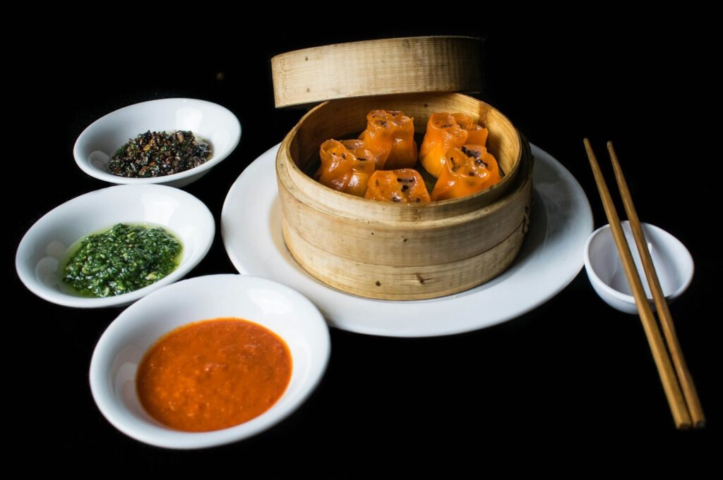 A bamboo steamer with assorted food and three bowls of sauce, highlighting vibrant food photography from Singapore.