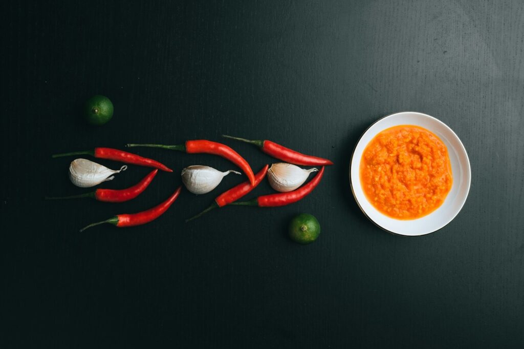 A bowl of vibrant chili sauce beside a plate of colorful peppers, elegantly styled for a food presentation.