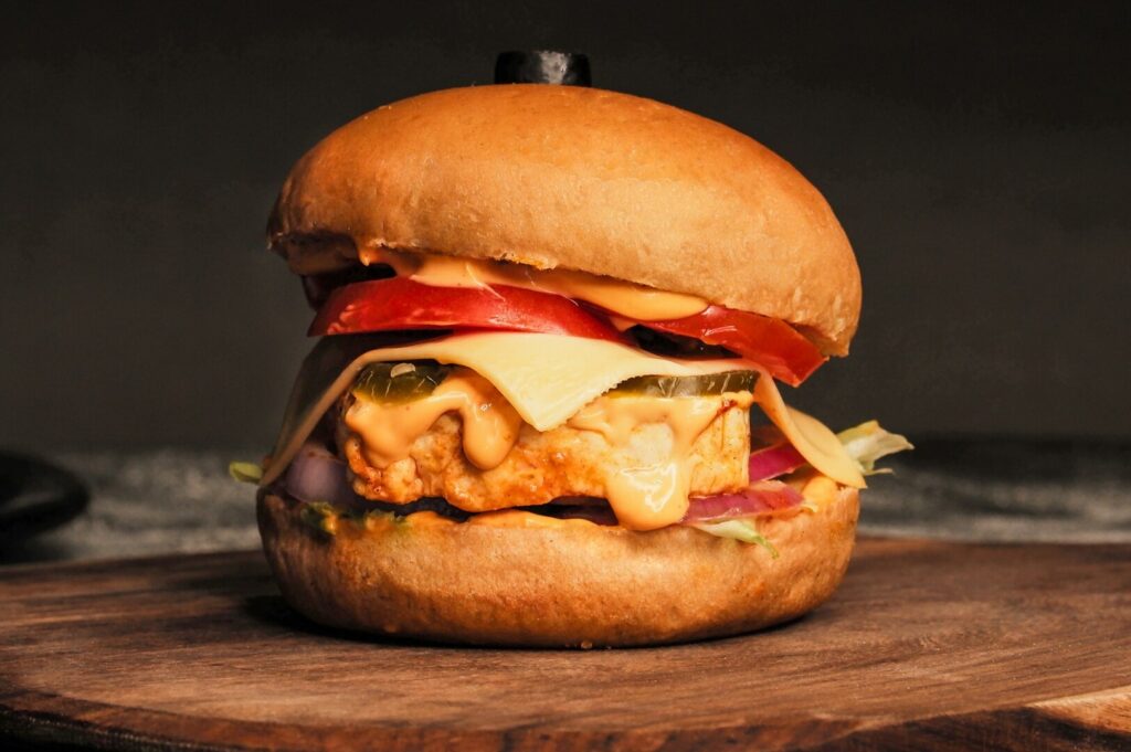 A styled hamburger with cheese, tomato, and onion presented on a rustic wooden board.
