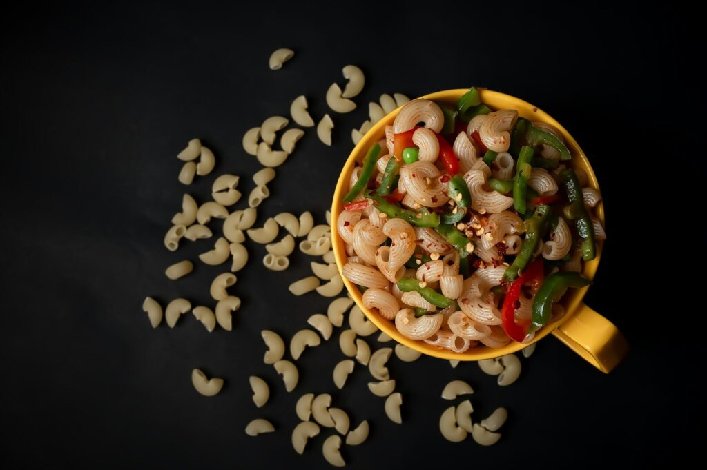 A beautifully styled bowl of pasta topped with colorful peppers and onions, showcasing vibrant food presentation.
