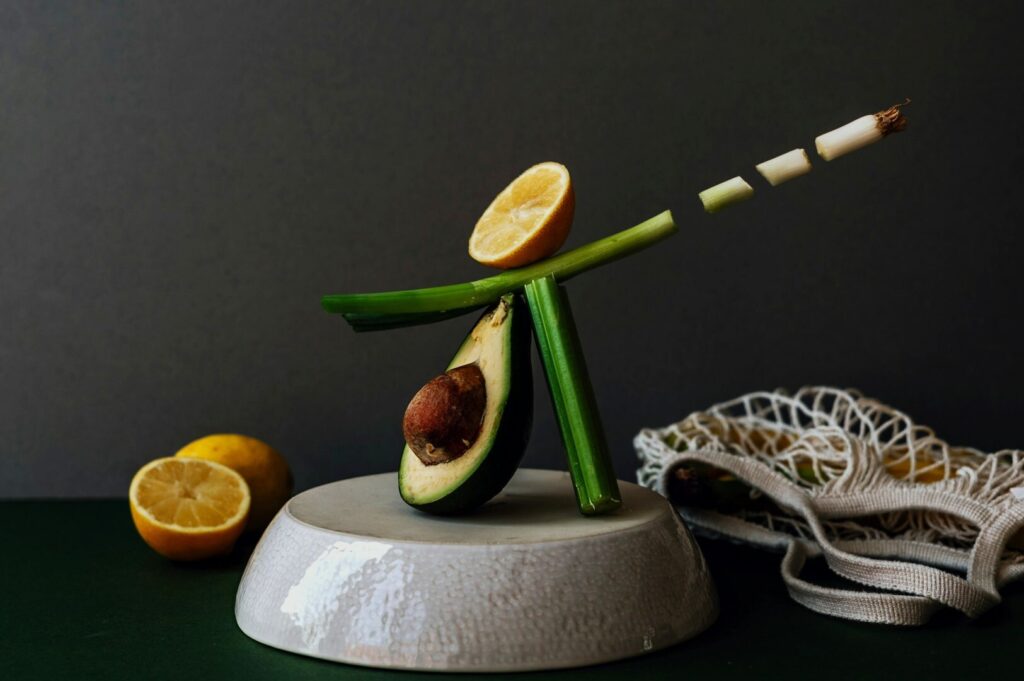A leek used as a stand holds a fresh avocado and lemon, highlighting their textures in a food photography composition.
