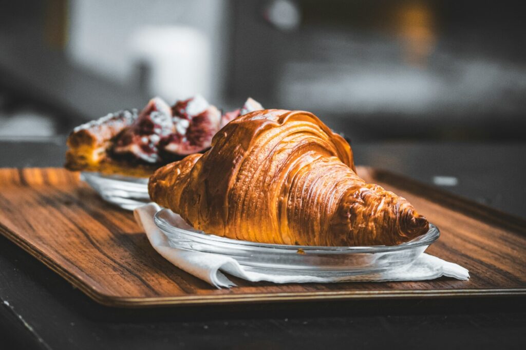 A beautifully styled croissant and pastry on a rustic wooden tray, showcasing professional food photography techniques.