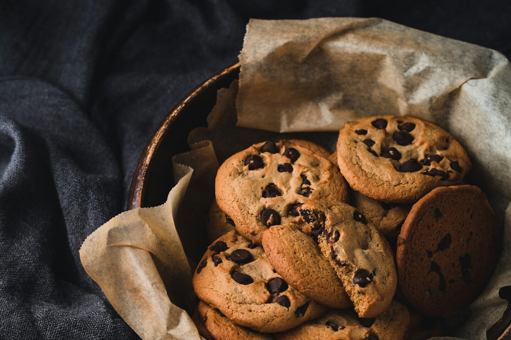A close-up of chocolate chip cookies arranged in a basket, set on a dark background, highlighting food photography.