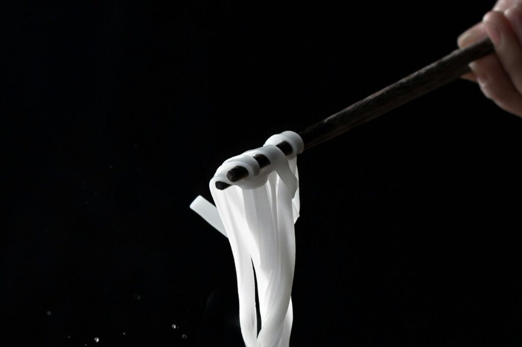 Close-up of a person using chopsticks to lift noodles from a bowl, highlighting the art of food photography.