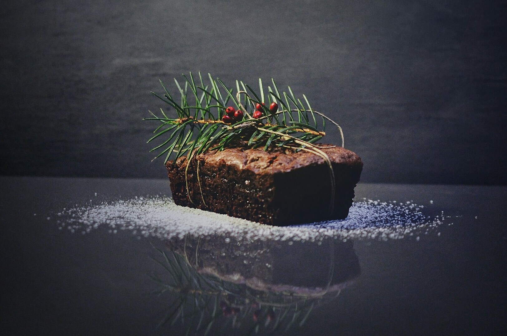A decadent chocolate cake slice adorned with pine needles, captured in a refined food photography setting.