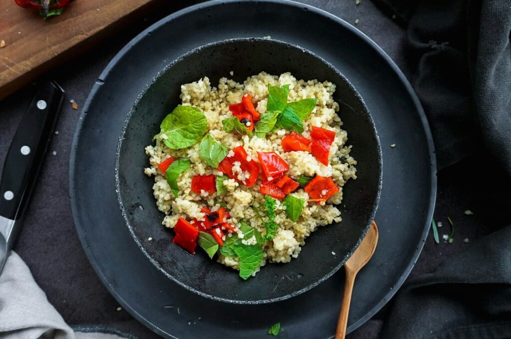 A vibrant dish of cauliflower rice garnished with red pepper and mint, captured in an appealing food photography setting.