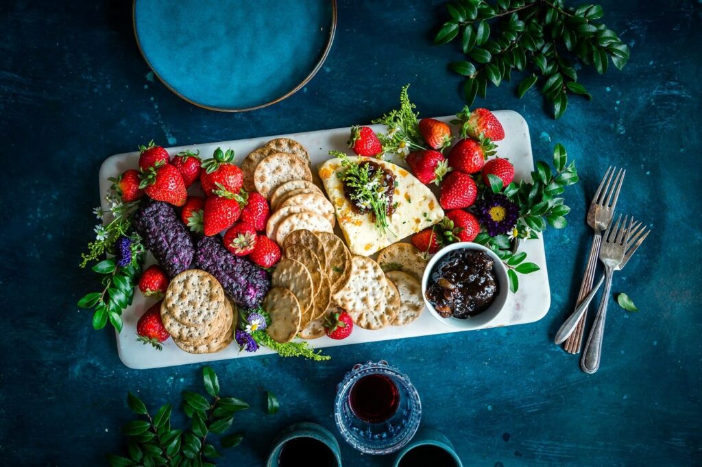 A beautifully arranged platter of assorted fruits and crackers accompanied by a glass of red wine.