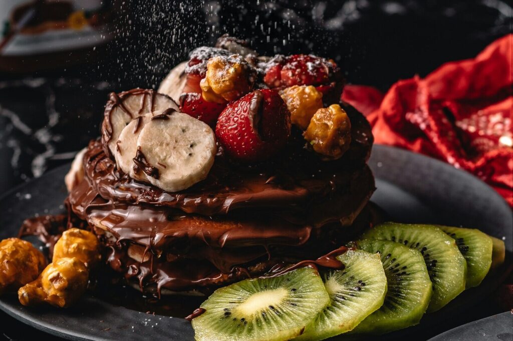 Chocolate pancakes topped with kiwi, bananas, and drizzled chocolate, beautifully styled for food photography.