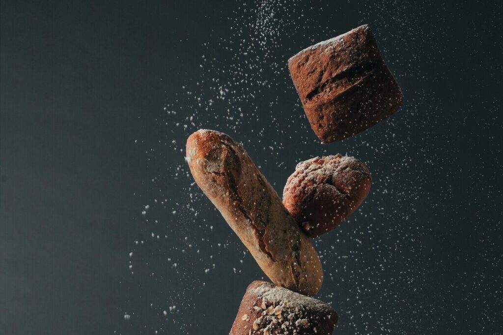Flour is sprinkled as a loaf of bread is thrown into the air, captured in an artistic food styling photograph.