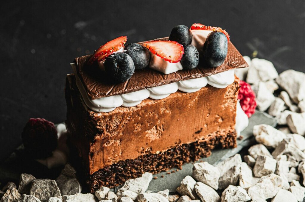 A decadent chocolate cake slice adorned with vibrant berries and strawberries, captured in elegant food styling.
