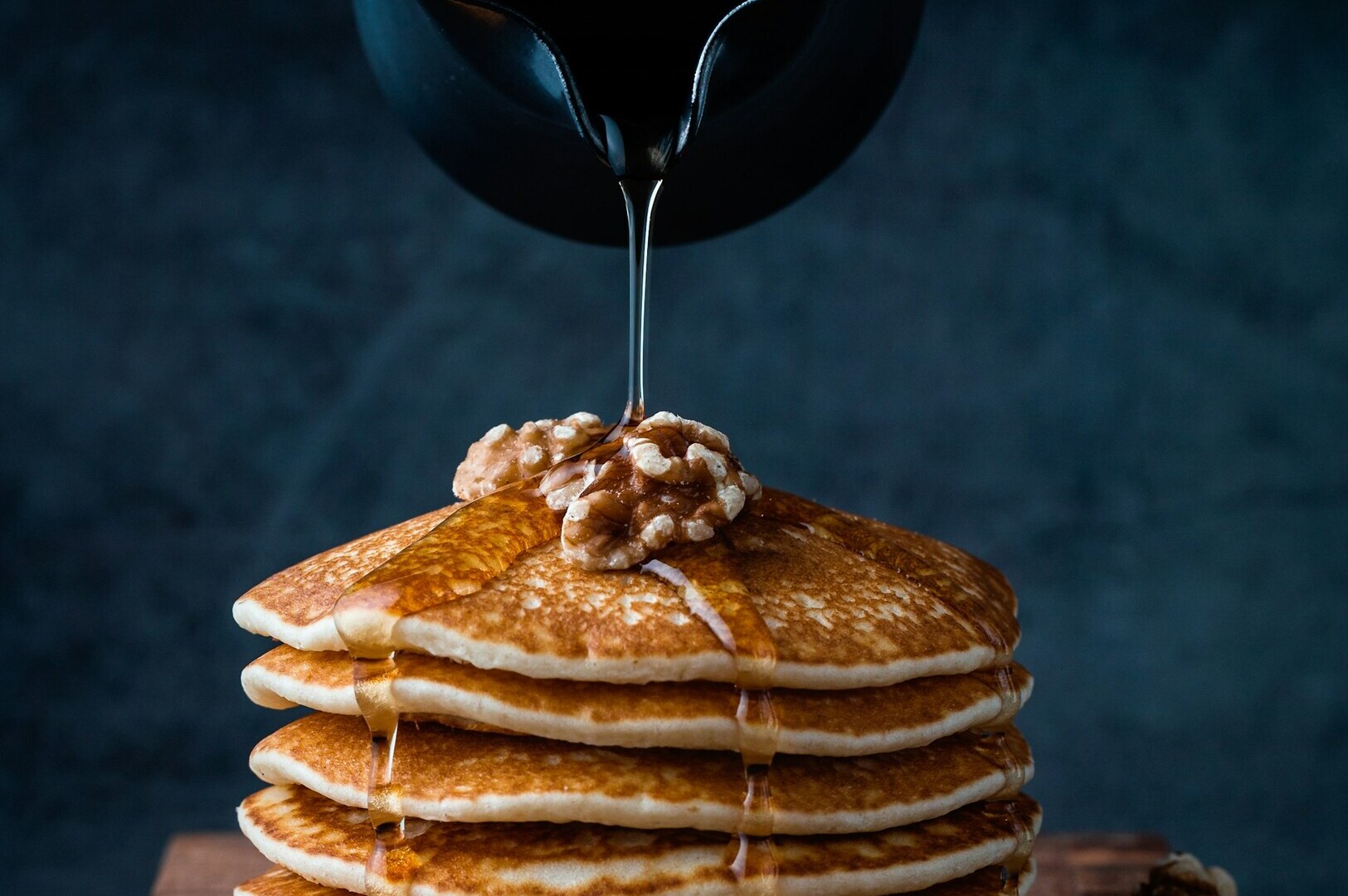 A stack of fluffy pancakes with golden syrup being poured over them, showcasing a delicious breakfast scene.