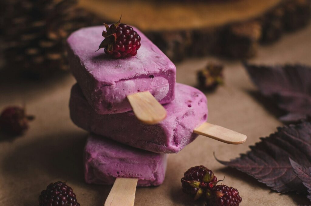 Colorful popsicles with berries and leaves arranged on a rustic wooden table, showcasing vibrant food photography.