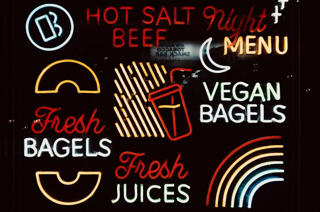 Bright neon sign showcasing a menu with hot salt, fresh bagels, and hot dogs, emphasizing food photography design.