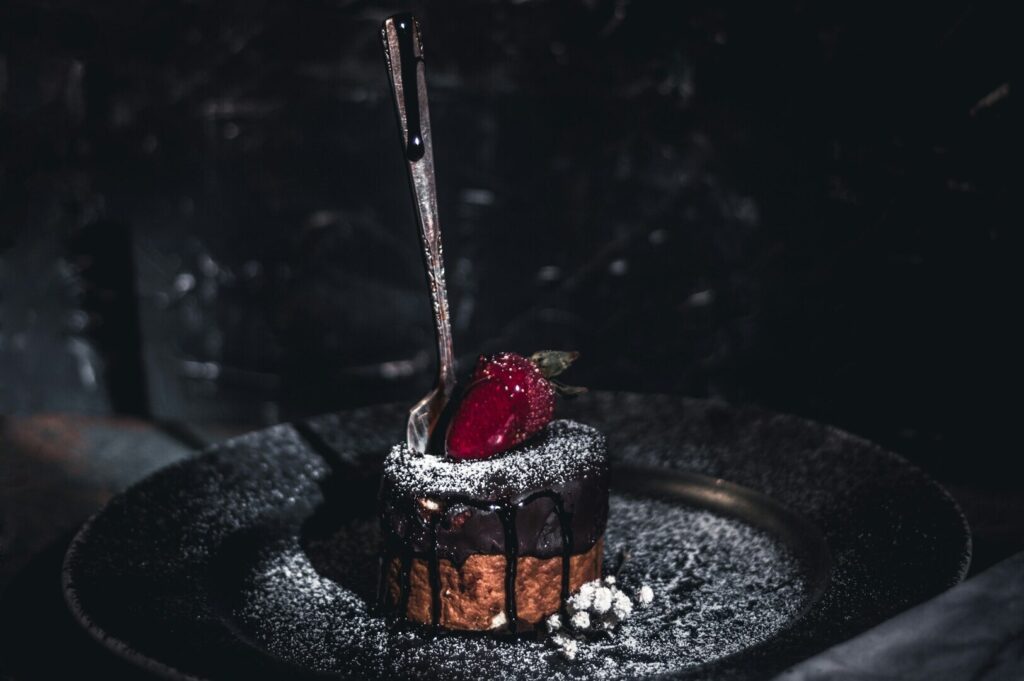 A black plate holds an elegant dessert accompanied by a silver spoon, showcasing food art photography.