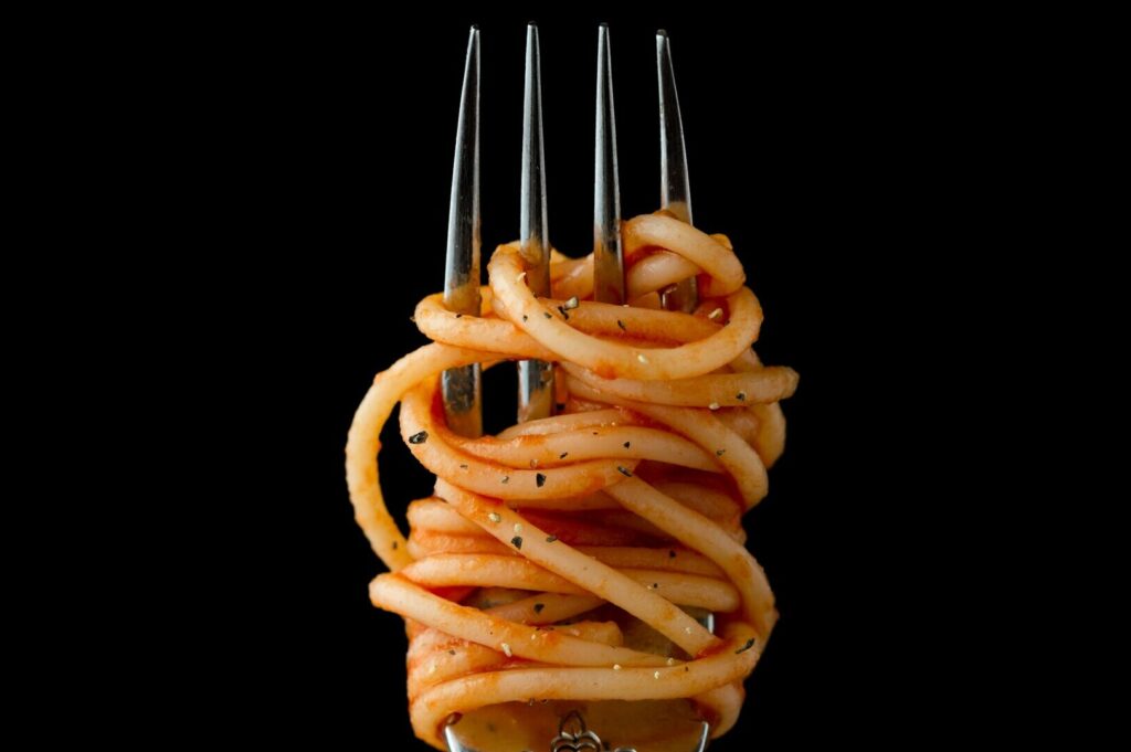 A close-up of a fork twirling spaghetti, showcasing the texture and shine of the pasta in a food photography setting.