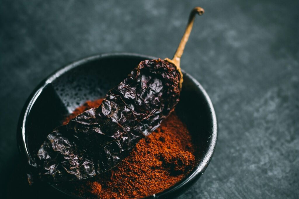 Close-up of a bowl containing chili powder, highlighting its deep red hue and fine texture in a food photography composition.