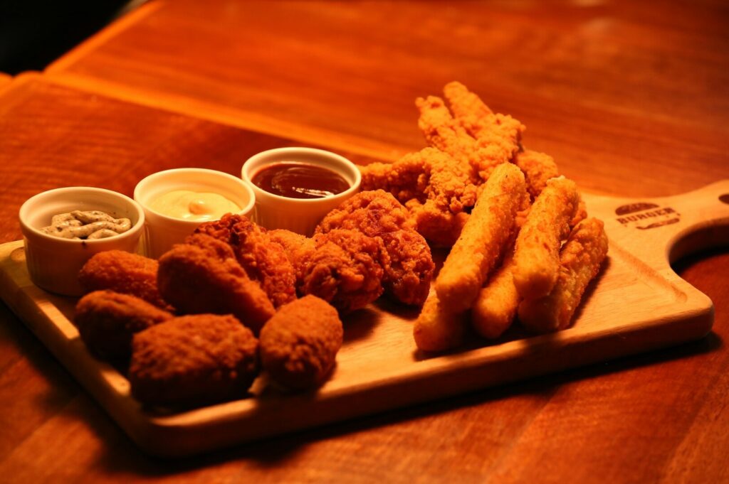 A wooden tray featuring crispy fried chicken, golden fries, and various dipping sauces, showcasing Singaporean food photography.