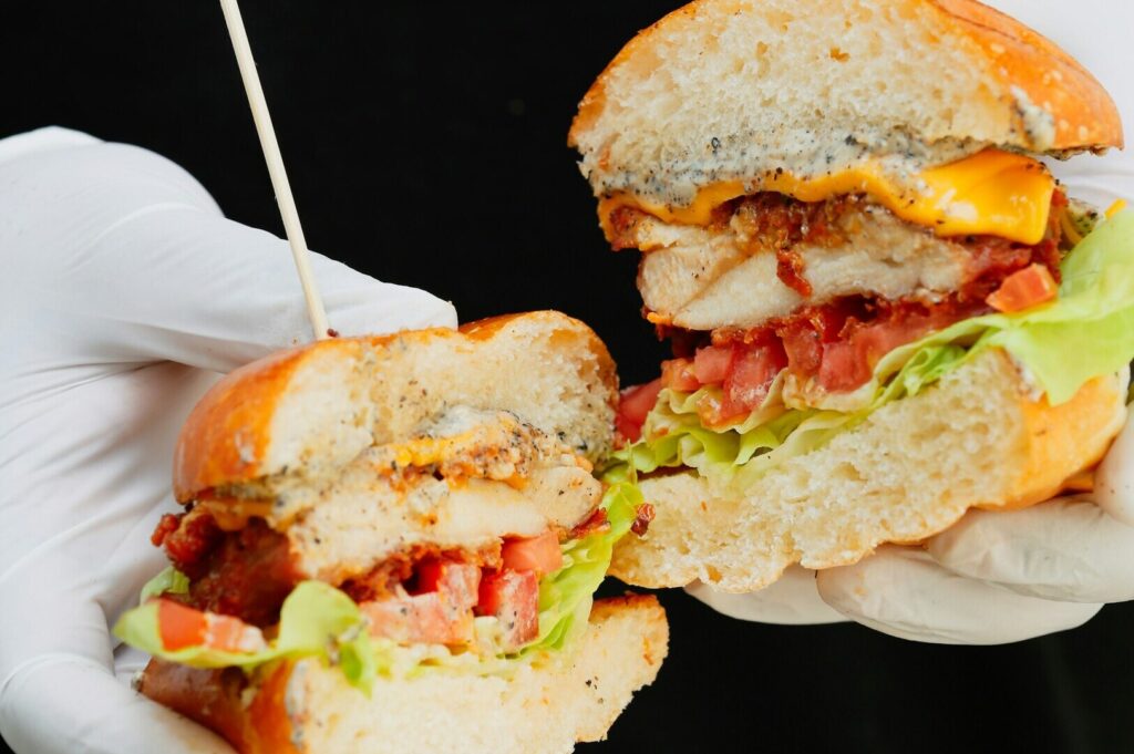 A hand gripping a sandwich with a stick, highlighting Singaporean culinary art in food photography.