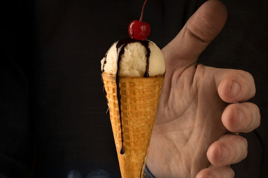 A man presents an ice cream cone adorned with a cherry on top, captured in a colorful food photography setting.