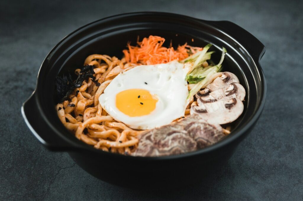 A close-up of a bowl of noodles garnished with a soft-boiled egg, highlighting the dish's textures in food photography.