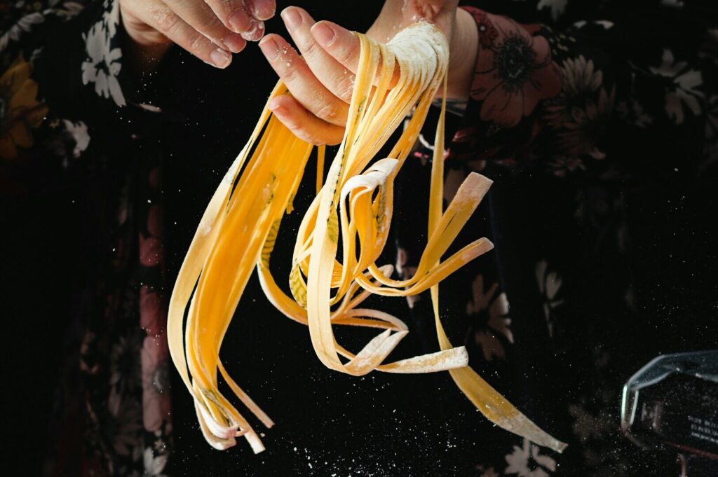 A woman delicately holds a spaghetti noodle, captured in an artistic food photography style.