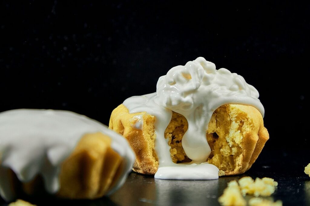 A muffin topped with icing beside a slice of cake, showcasing vibrant colors in a food art photography style.