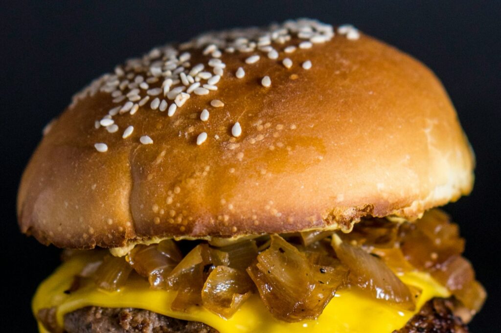Close-up of a burger with a sesame seed bun, topped with caramelized onions and melted cheese, showcasing a juicy beef patty. Rich and appetizing.