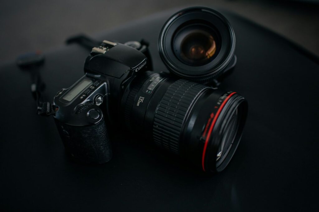 A DSLR camera with a zoom lens lies on a dark surface. The camera's body and lens feature detailed markings, while the overall mood is sleek and professional.