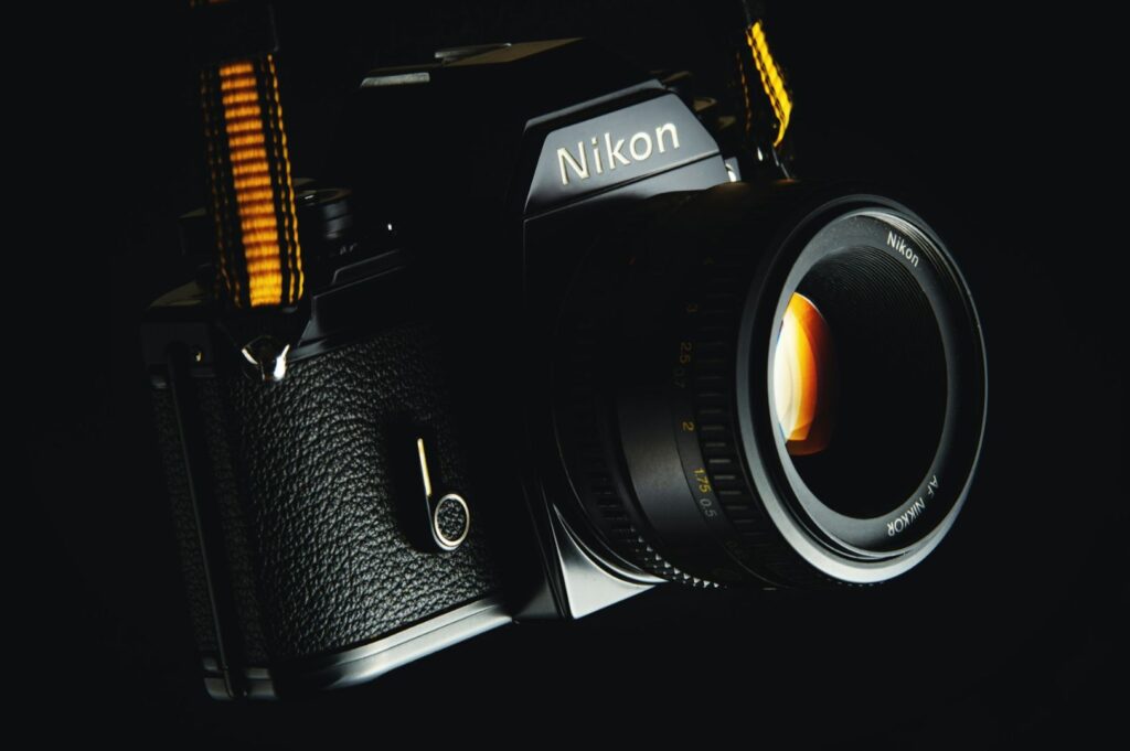 Close-up of a vintage Nikon camera with a textured black body, gleaming lens, and yellow strap, set against a dark background, evoking a classic, nostalgic tone.