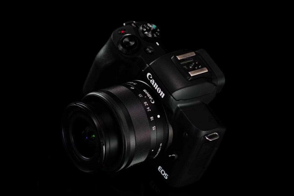 A Canon EOS camera with a lens attached is positioned on a black background. The camera is angled slightly to the right, showcasing its matte finish and lens details.
