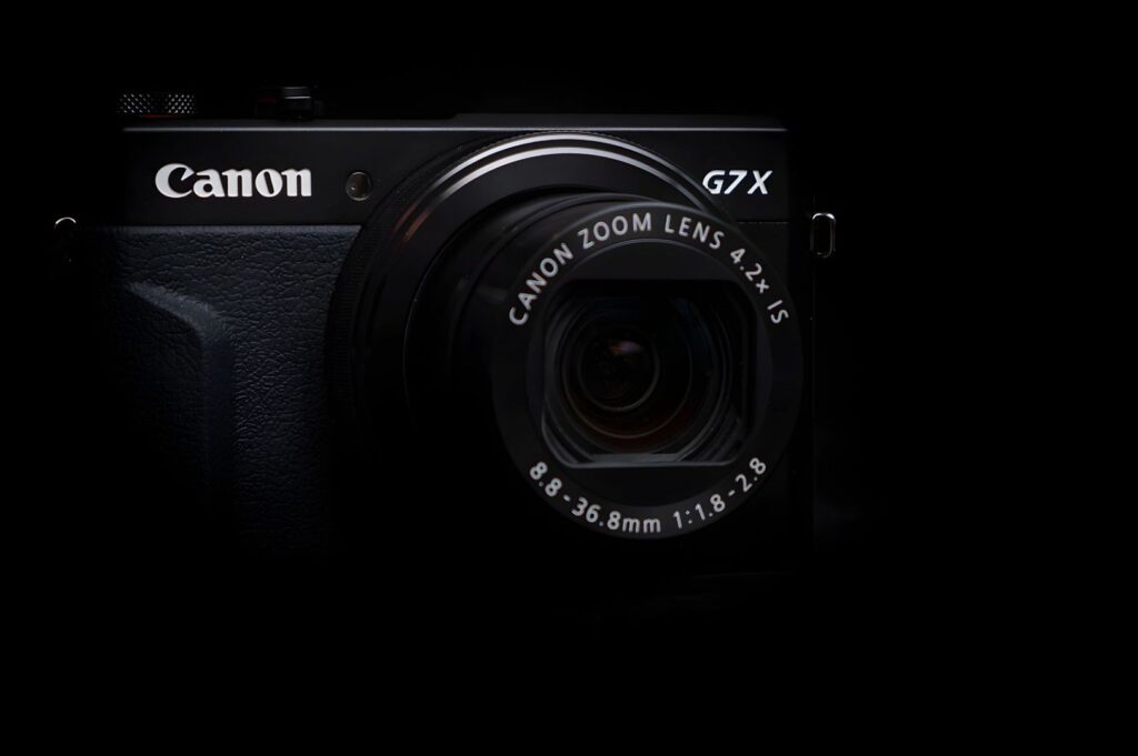 Close-up of a Canon G7 X camera with a visible zoom lens, set against a dark background. The image conveys a sleek and professional tone.