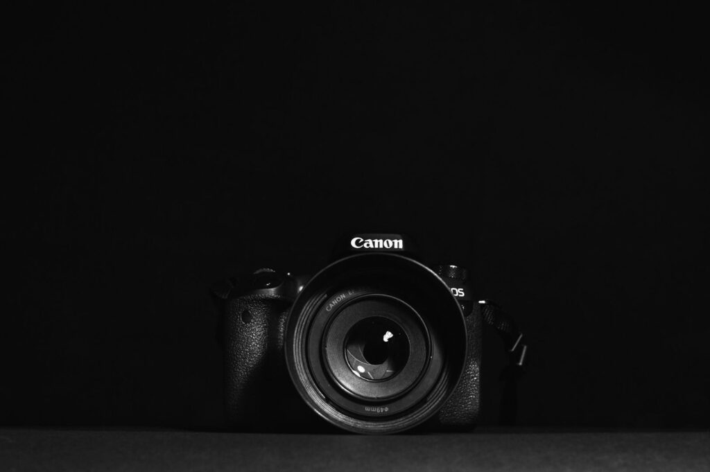 A Canon camera with a prominent lens is centered against a solid black background, creating a minimalist and focused composition.