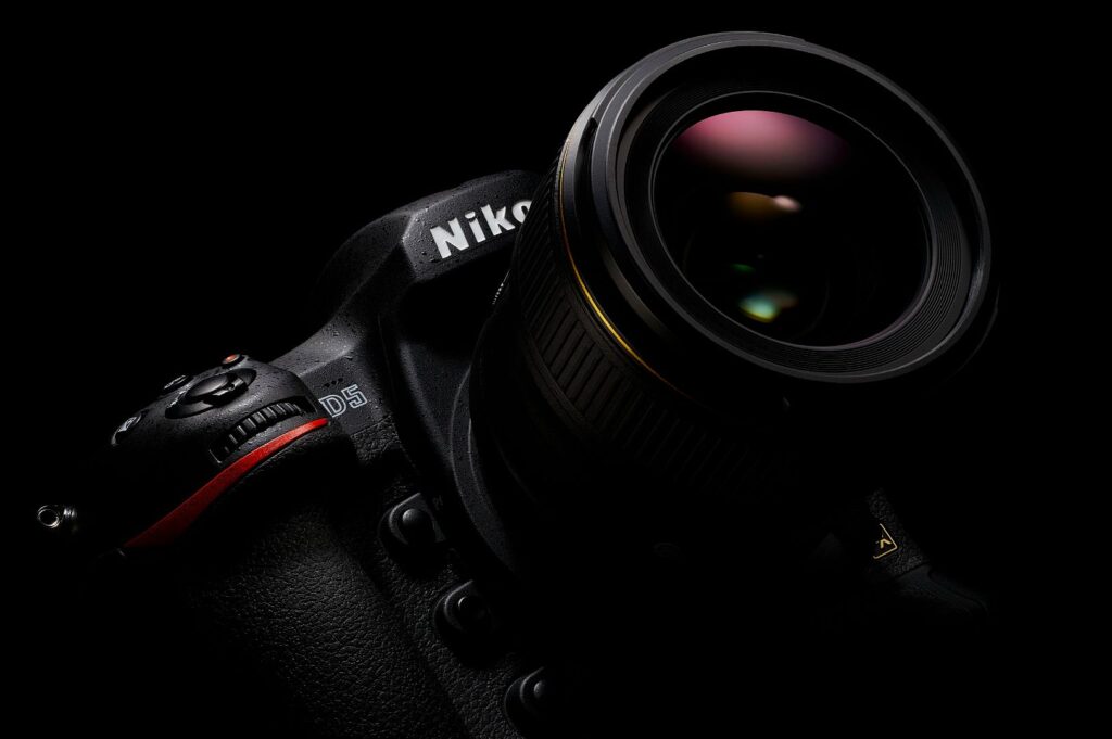 Close-up of a Nikon DSLR camera against a black background. The lens has a subtle, colorful reflection, highlighting the camera's sleek design.