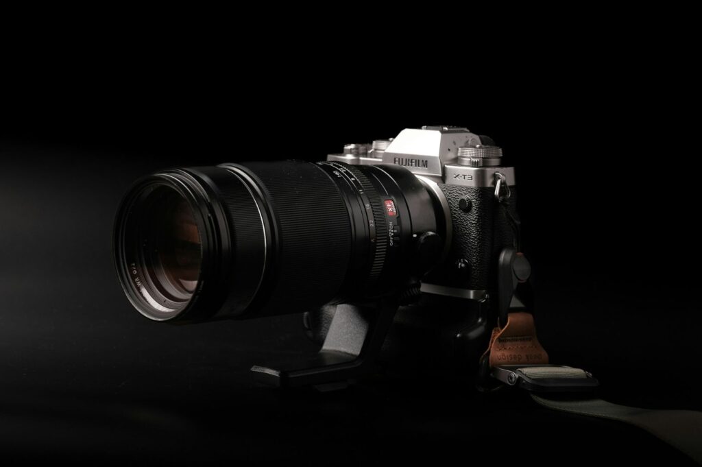 A silver and black Fujifilm X-T3 camera with a large zoom lens is positioned against a dark background, emphasizing its sleek design and modern technology.