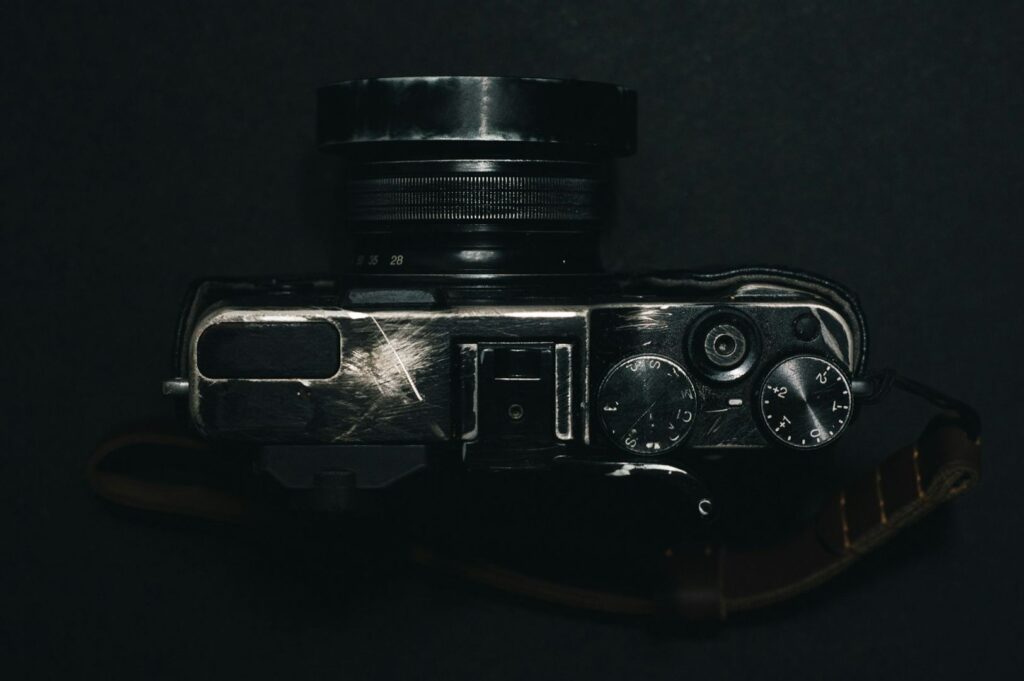Top view of a vintage, well-worn camera against a dark background. The camera has visible scratches and metal dials, evoking a sense of nostalgia.