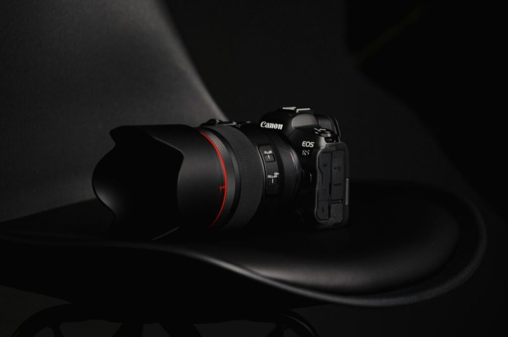 A Canon EOS R5 camera with a large lens rests on a sleek black chair. The dark setting and soft lighting create a modern, professional tone.