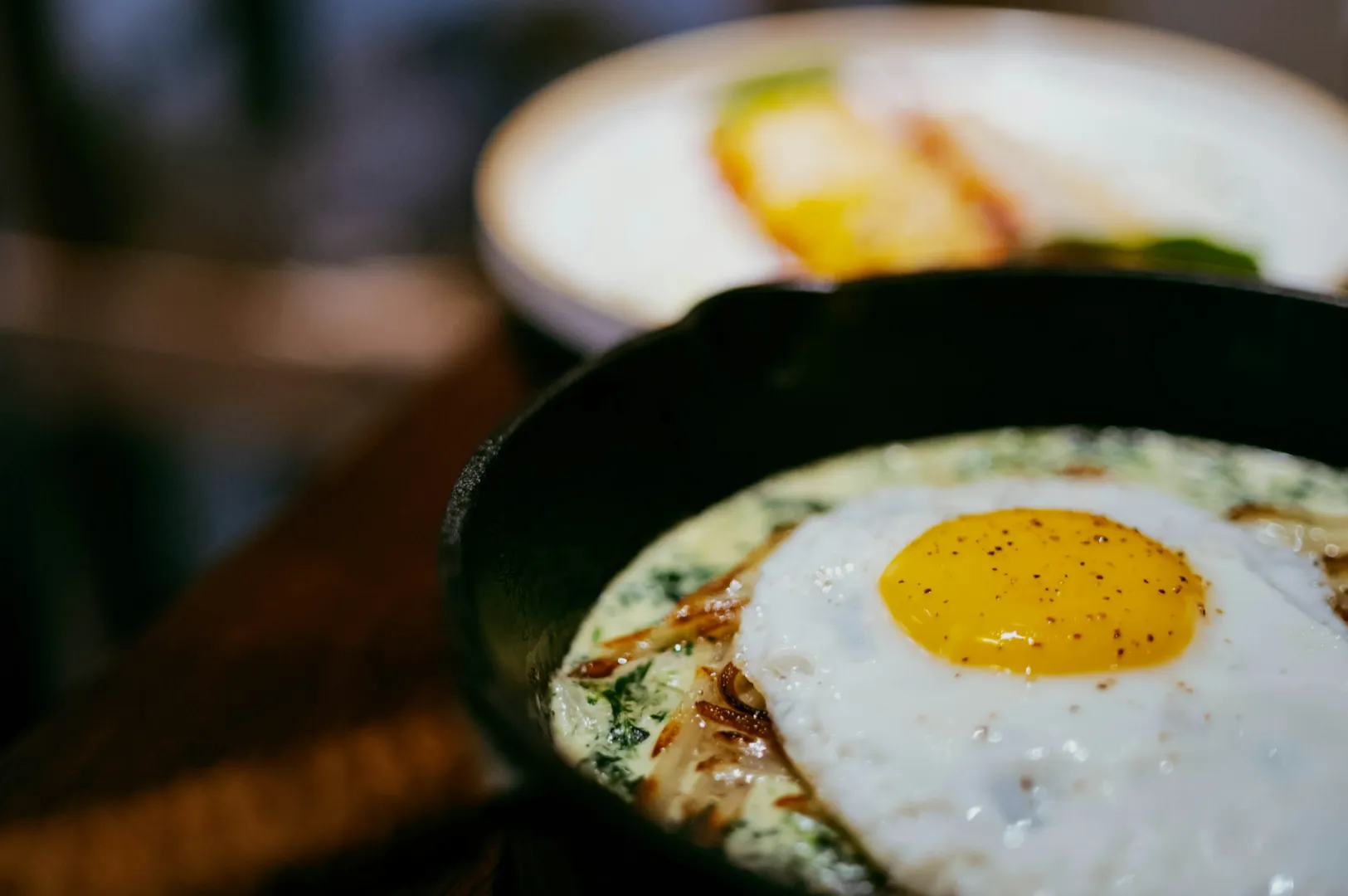 A black bowl of ramen with creamy broth, topped with a slice of pork, green onions, wood ear mushrooms, and a wooden spoon, creating a warm, savory tone.