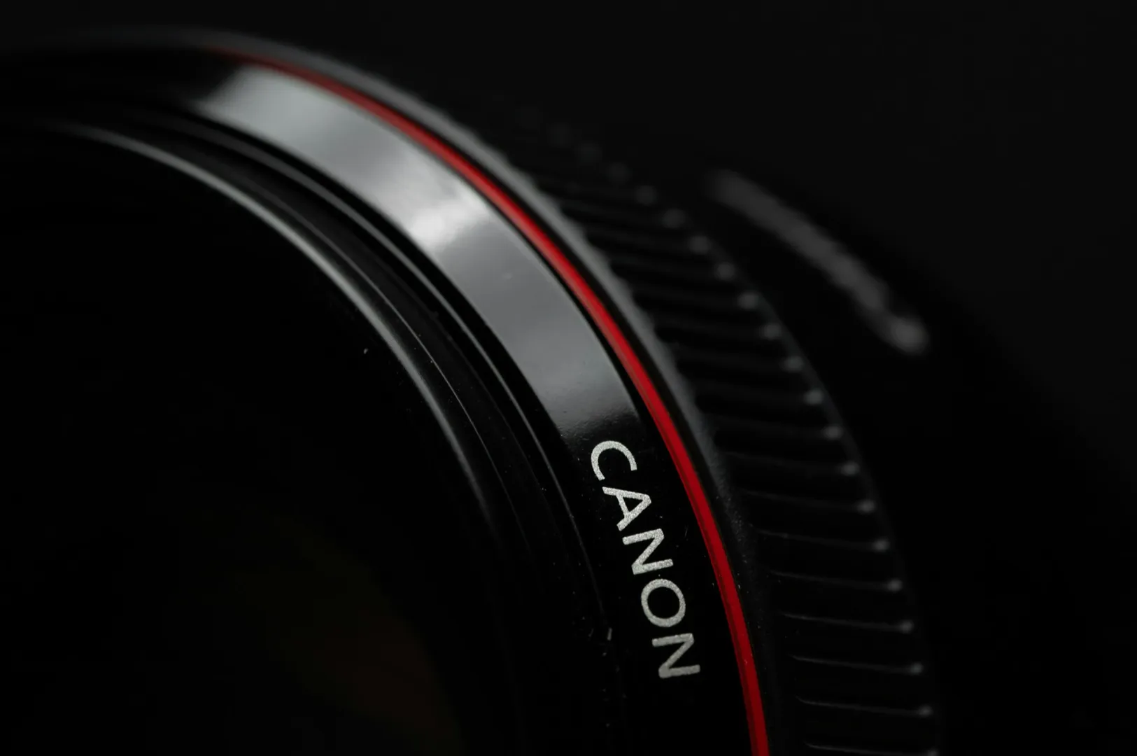 Close-up of a Canon camera lens showing a sleek black surface with a thin red ring, highlighting the brand name in white for a professional look.