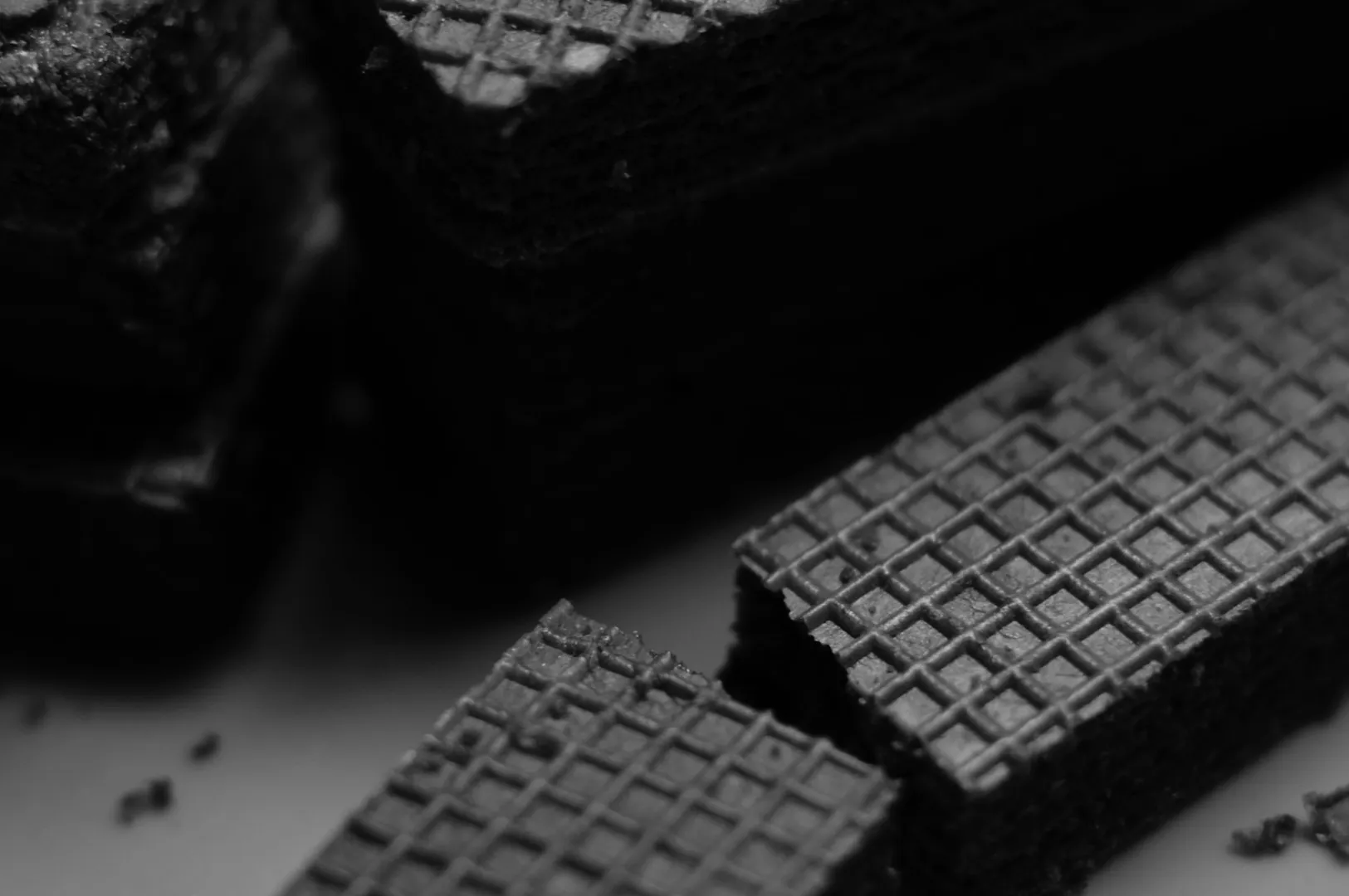 Close-up of stacked chocolate wafers, highlighting their textured grid pattern. The monochrome tone evokes a rich, indulgent feel.