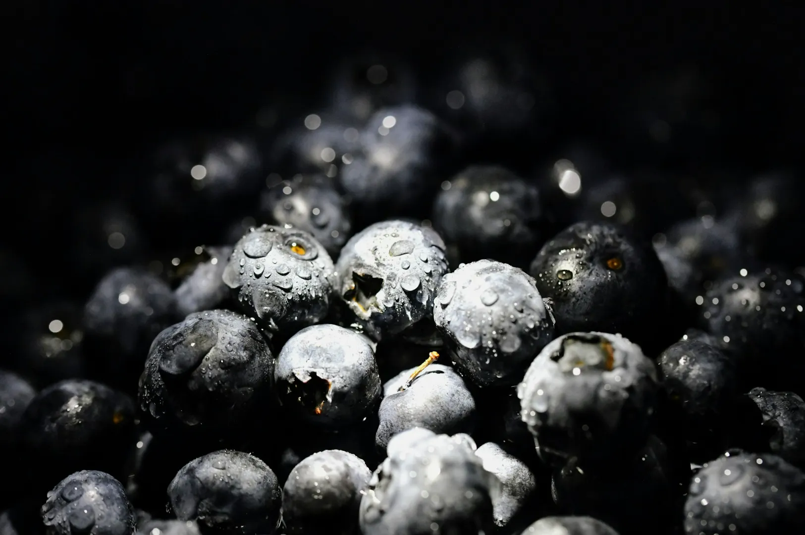 Close-up of fresh blueberries with water droplets in dim lighting, creating a moody and inviting atmosphere. The berries are dark and glossy.