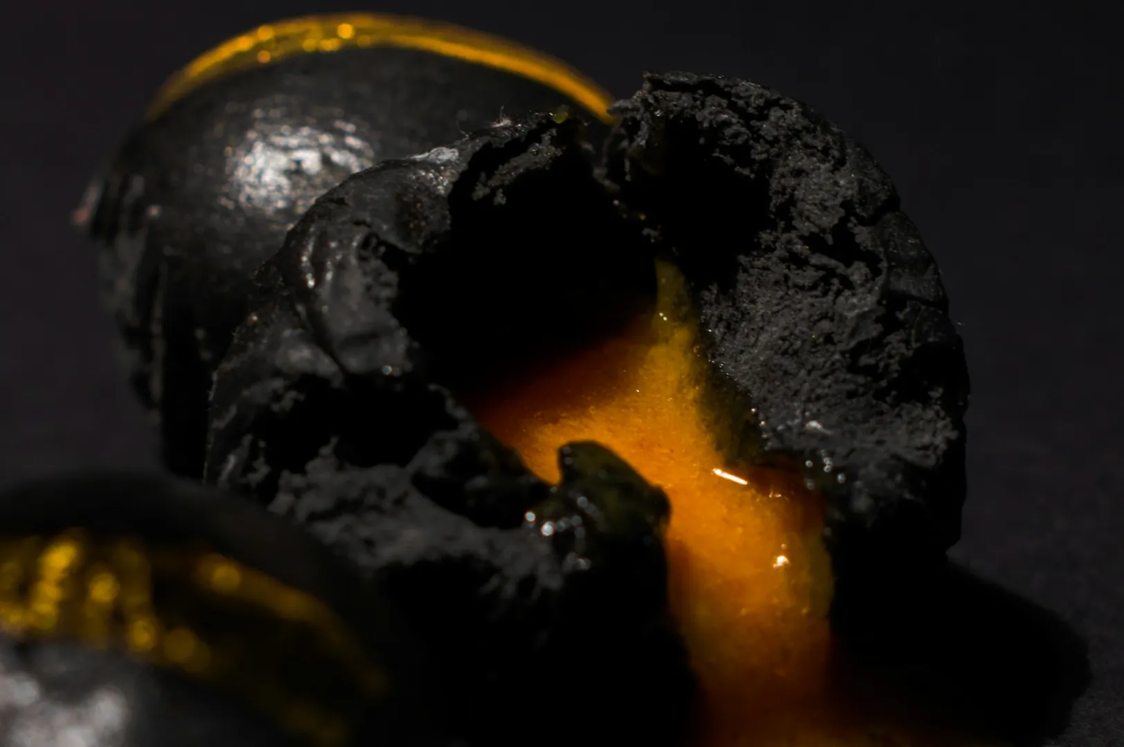 “Black dumplings with vibrant orange filling oozing out on a dark surface, creating a dramatic contrast. The scene feels rich and indulgent.”
